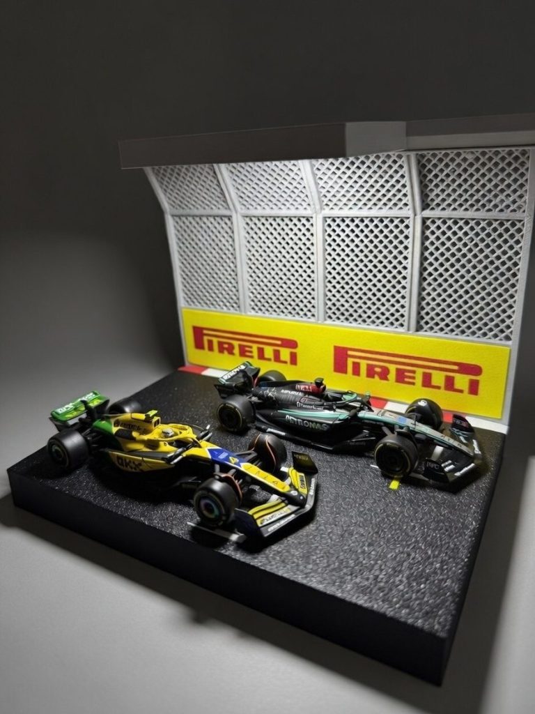 Bburago Formel-1-Modelle Drei Formel-1-Modellautos stehen vor einer Pirelli-Wand mit Gitterstruktur.
