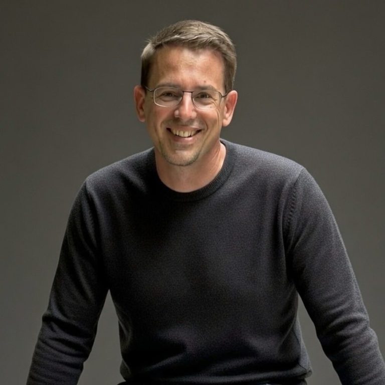 Michael Nimphius Lächelnder Mann in einem schwarzen Pullover vor neutralem Hintergrund.