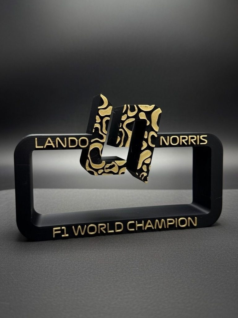 Lando Norris F1 World Champion Schwarzer Aufsteller mit goldenen Verzierungen und der Inschrift "Lando Norris F1 World Champion".